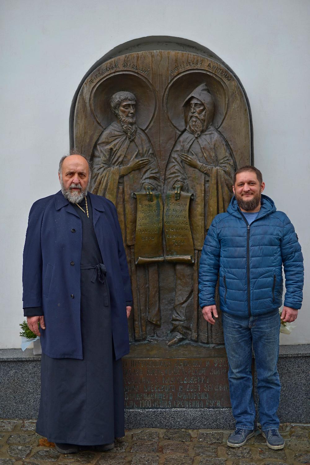 Киево-Печерская лавра, батюшка с пономарем на фоне преподобного Антония и Феодосия Печерских, памятник преподобным